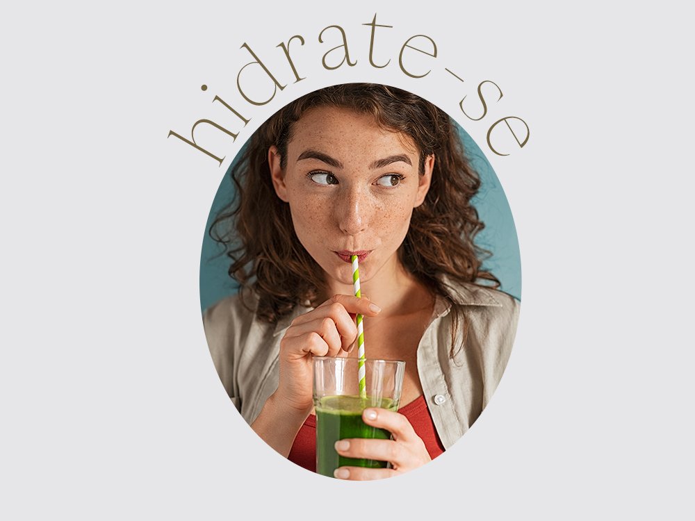 Mulher bebendo suco verde em um copo de vidro e com canudo e na imagem escrito a palavra "hidrata-se".