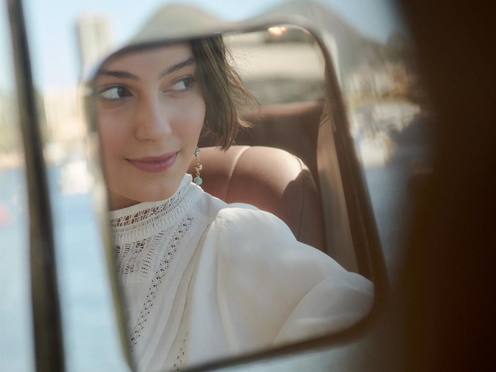 mulher refletida no espelho retrovisor do carro com rio de janeiro ao fundo