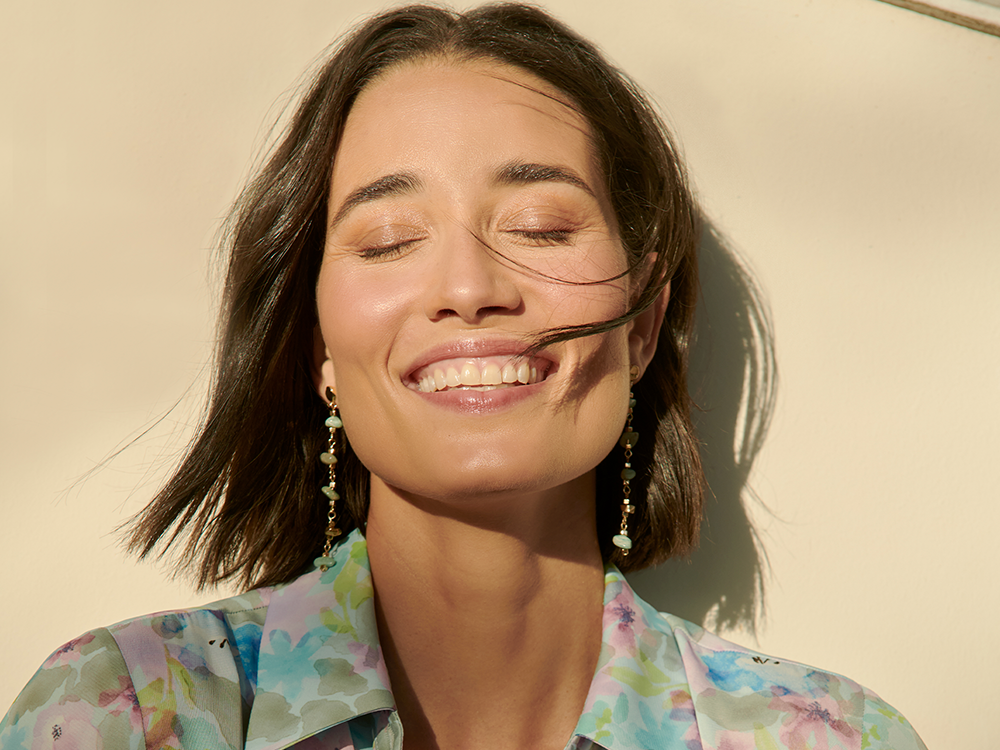 mulher bonita morena sorri ao sol de olhos fechados